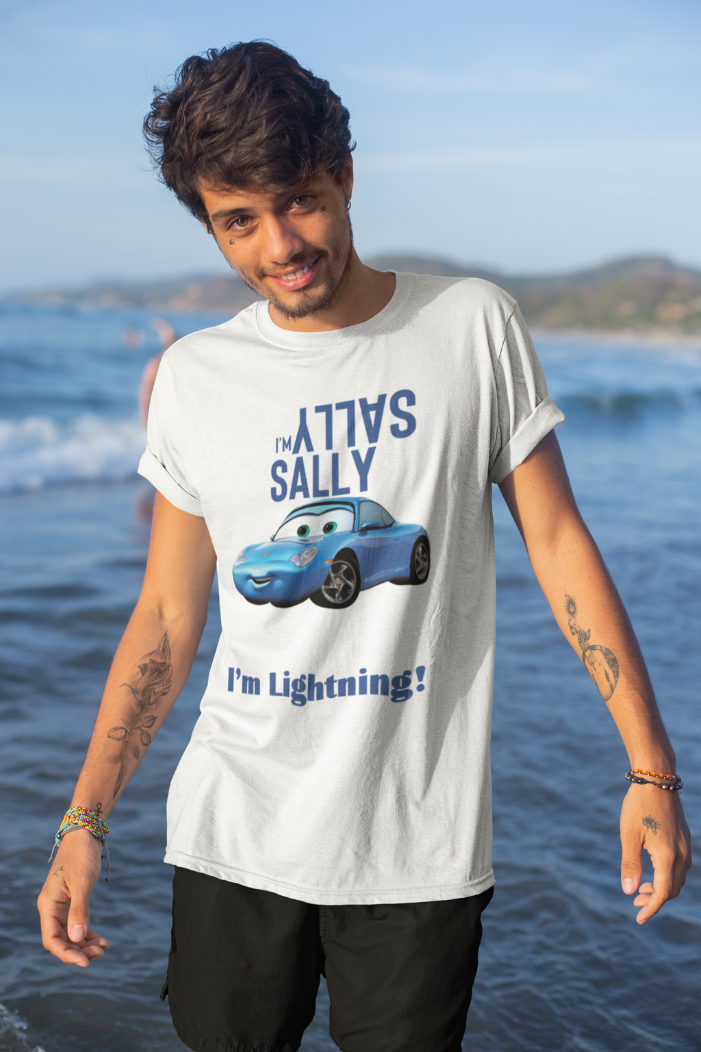 Person wearing a white t-shirt with a graphic and text, standing by the ocean.