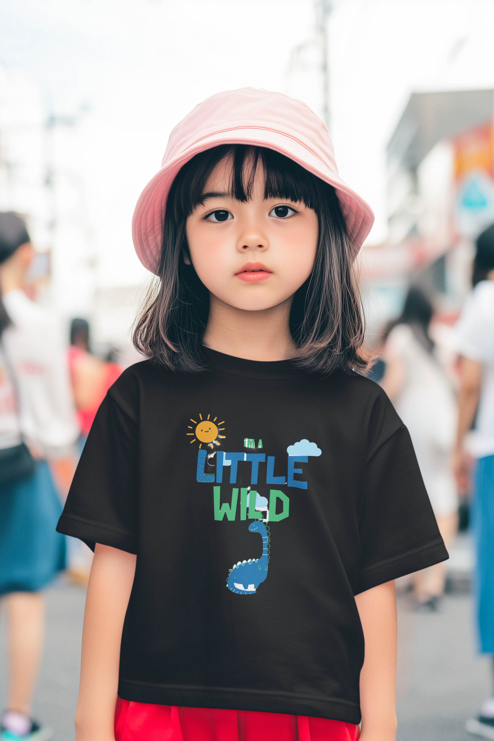 Child wearing a black t-shirt with 'LITTLE WILD' design and a pink hat in an outdoor setting.